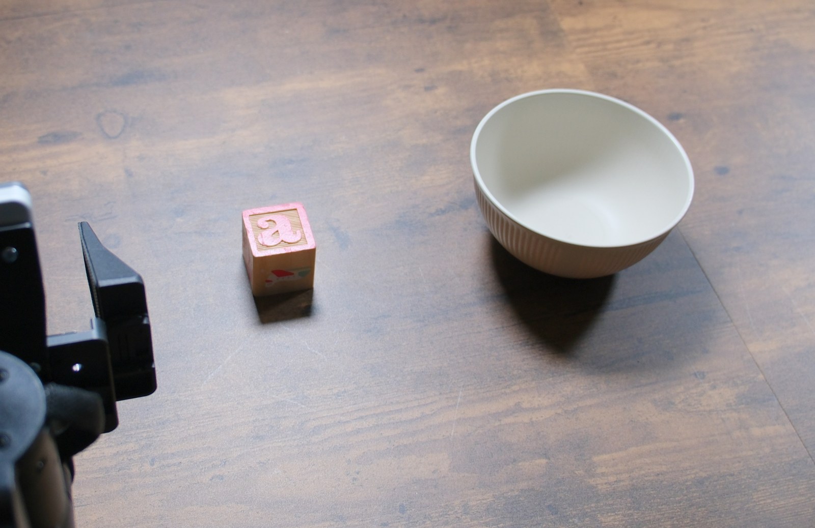 The bowl task set up on the rig: a small wooden block on the
      table beside an empty bowl, with one gripper at the left edge of frame.